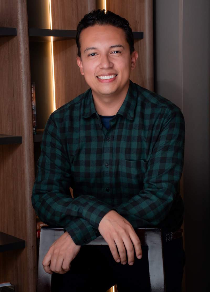 Christian F. Rojas leaning on the back of a chair, smiling.